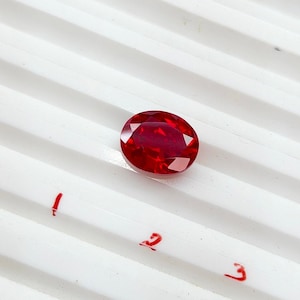 May include: A deep red oval-shaped gemstone on a white background with the numbers 1, 2, and 3 written in red.