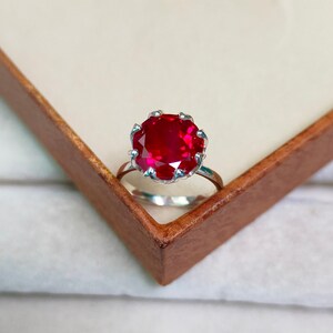 Puede incluir: Un anillo de plata con una gran piedra preciosa de rubí rojo redonda engastada en un engaste en forma de corona.