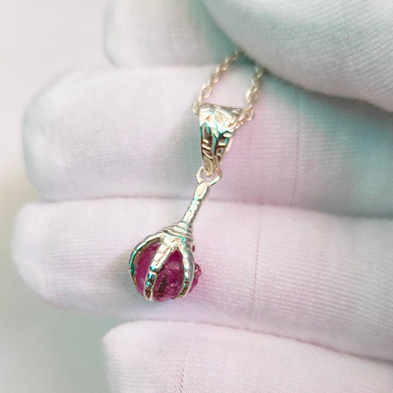 May include: A silver pendant necklace with a pink gemstone held in a claw-like design.
