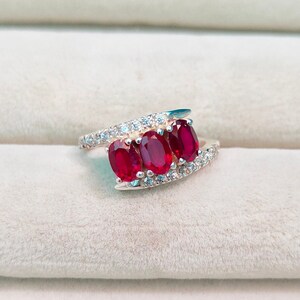 May include: A silver ring with three oval-shaped red gemstones and a row of small white gemstones.