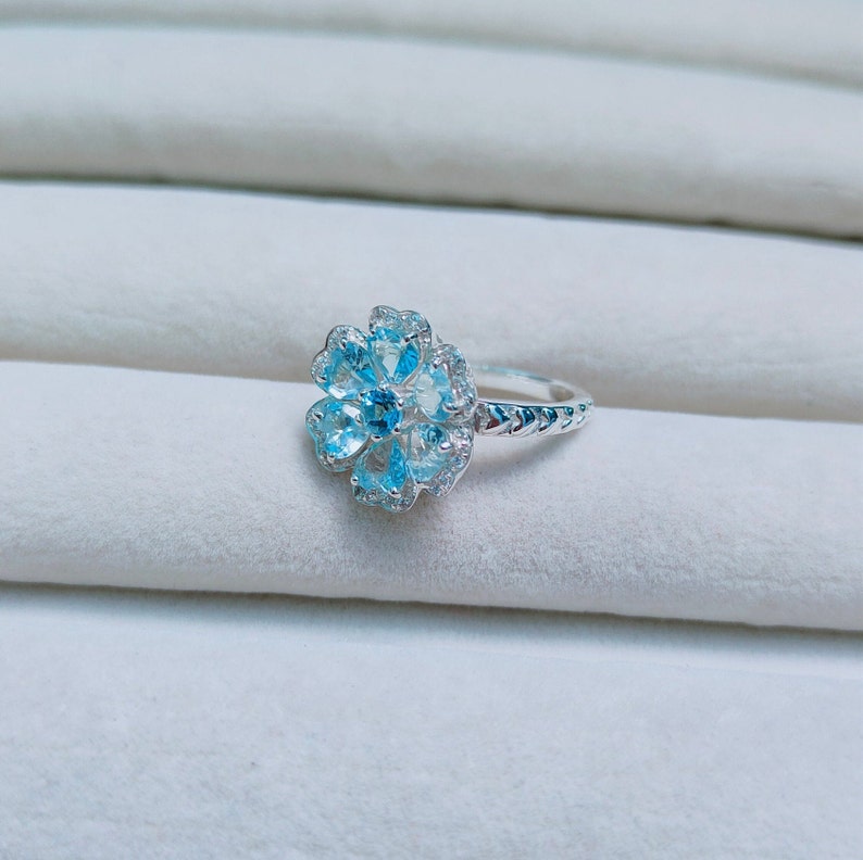 May include: A silver ring with a blue topaz flower design. The ring has a delicate band and a cluster of blue topaz stones set in a flower shape.