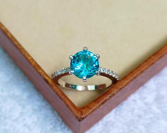 Puede incluir: Un anillo de plata con una gran piedra preciosa redonda azul turquesa rodeada por una banda de piedras preciosas más pequeñas y transparentes.