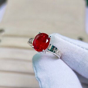 Puede incluir: Un anillo de plata con una gran piedra preciosa de rubí de forma ovalada. El anillo tiene un diseño delicado e intrincado.
