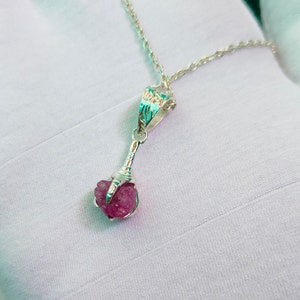 May include: A silver necklace with a pink gemstone pendant. The pendant is a raw, uncut stone held in a silver claw setting.