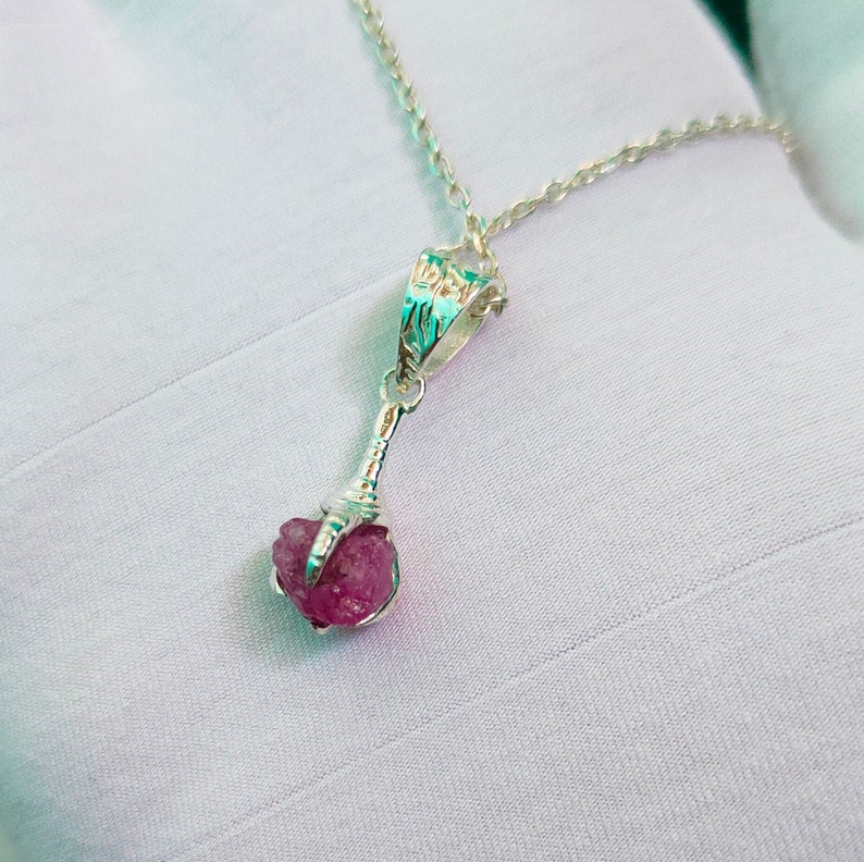May include: A silver necklace with a pink gemstone pendant. The pendant is a raw, uncut stone held in a silver claw setting.
