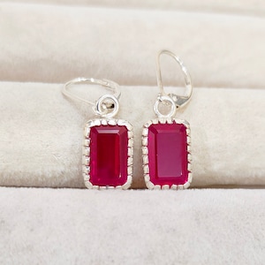 May include: A pair of silver dangle earrings with red rectangular gemstones.