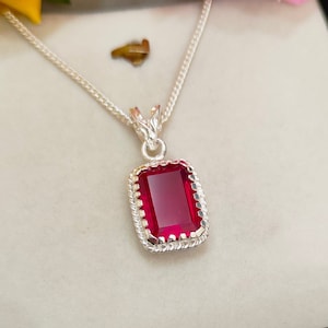 May include: A silver chain necklace with a pendant featuring a red gemstone set in a silver frame.