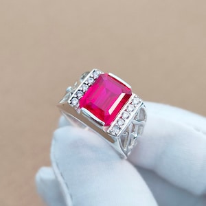 May include: A silver ring with a large, rectangular, red gemstone surrounded by smaller, clear gemstones.