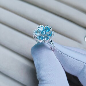 May include: A silver ring with a flower-shaped design featuring blue gemstones and smaller clear gemstones.