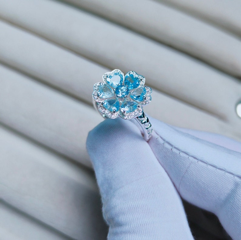 May include: A silver ring with a flower-shaped design featuring blue gemstones and smaller clear gemstones.