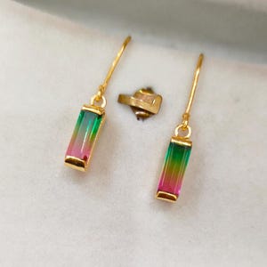 Puede incluir: Un par de pendientes de oro con una piedra preciosa rectangular multicolor. La piedra preciosa es verde, rosa y amarilla.