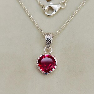May include: A silver chain necklace with a heart-shaped pendant featuring a red gemstone.