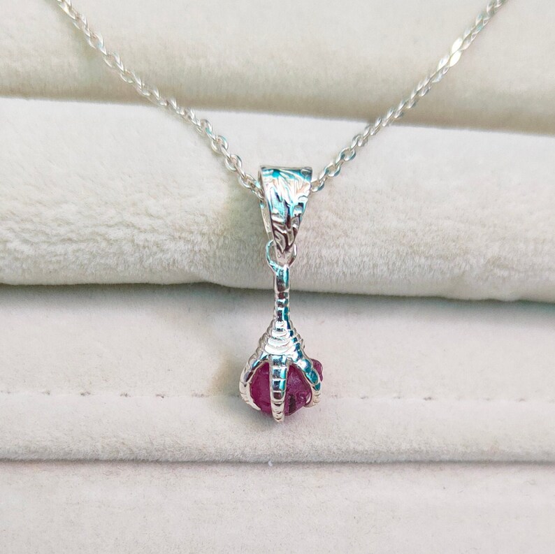 May include: A silver necklace with a pink gemstone pendant shaped like a claw.