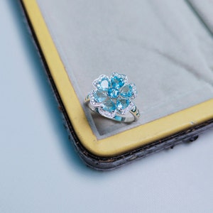 May include: A silver ring with a flower-shaped design featuring blue gemstones and smaller white gemstones.