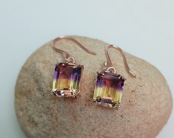 May include: A pair of rose gold earrings with a purple, yellow, and orange gemstone in an emerald cut.