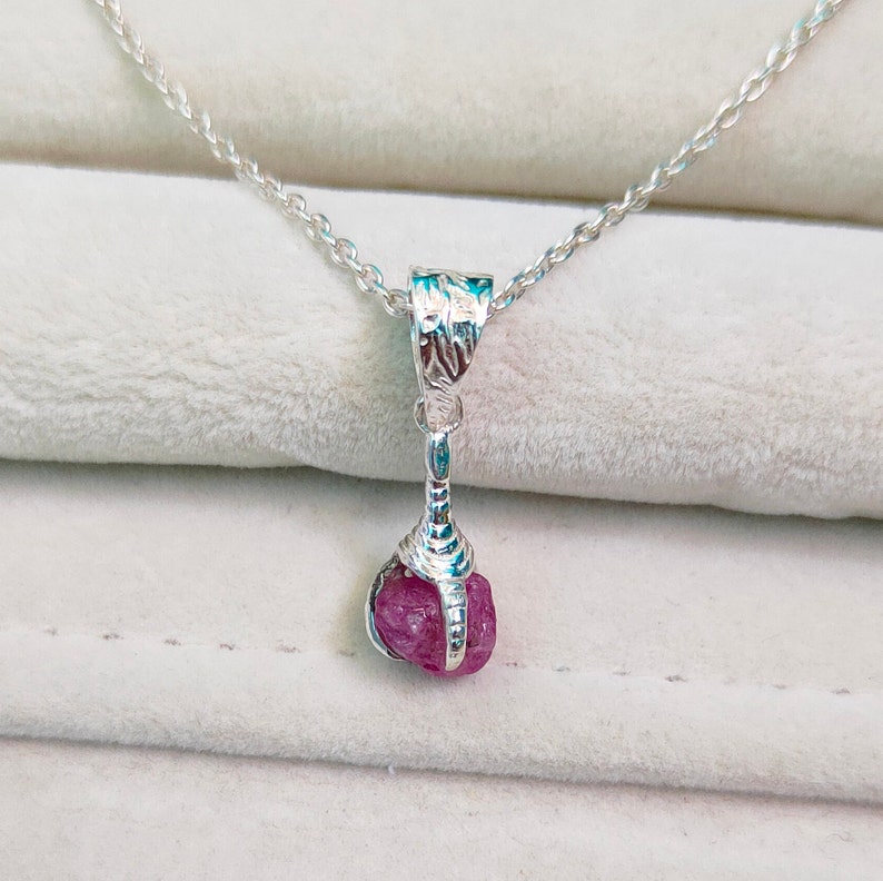 May include: A silver necklace with a pink gemstone pendant. The pendant is set in a silver claw setting.