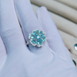 May include: A silver ring with a flower design featuring blue gemstones and white accents.