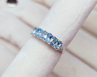 May include: A silver band ring with a row of oval-shaped blue topaz gemstones.