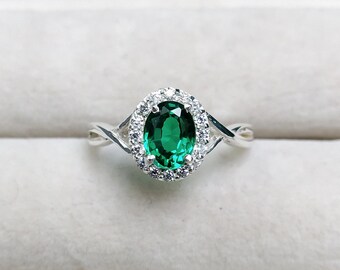 May include: A silver ring featuring a large oval green gemstone encircled by a halo of smaller clear gemstones.