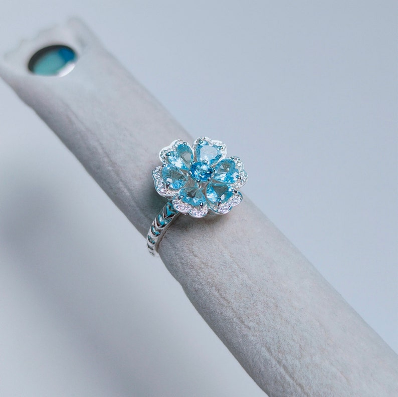 May include: A silver ring with a blue topaz flower design. The ring has a textured band and a flower-shaped setting with multiple blue topaz stones.