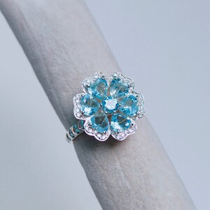 May include: A silver ring with a blue topaz flower design. The ring features a cluster of blue topaz stones set in a silver flower shape.