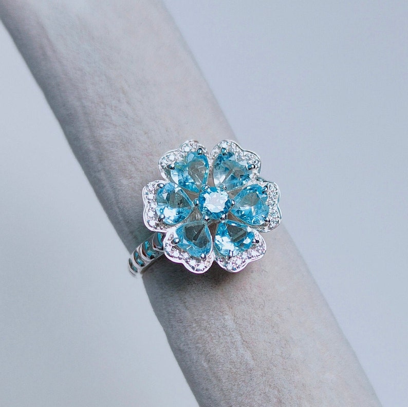 May include: A silver ring with a blue topaz flower design. The ring features a cluster of blue topaz stones set in a silver flower shape.