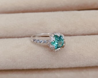 Puede incluir: Un anillo de plata con una gran piedra preciosa redonda de color turquesa rodeada de pequeñas piedras preciosas transparentes.