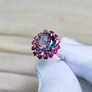 Op de afbeelding: Een zilveren ring met een grote ovale edelsteen omringd door kleinere roze edelstenen.