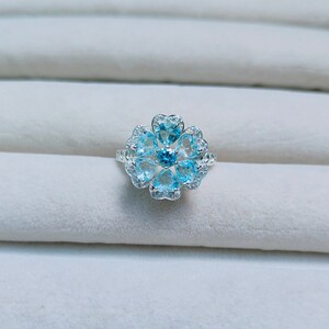 May include: A silver ring with a blue topaz center stone and smaller blue topaz stones set in a flower shape.