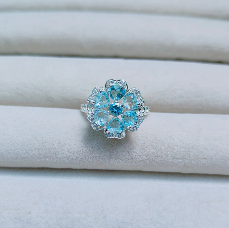 May include: A silver ring with a blue topaz center stone and smaller blue topaz stones set in a flower shape.
