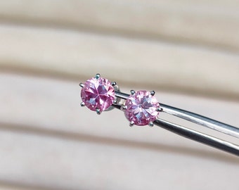 Pode incluir: Um par de brincos de prata com pedras redondas cor-de-rosa.
