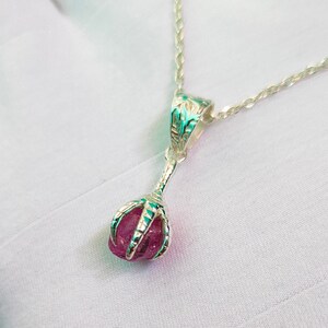 May include: A silver necklace with a pink gemstone pendant. The pendant is held in a silver claw design.