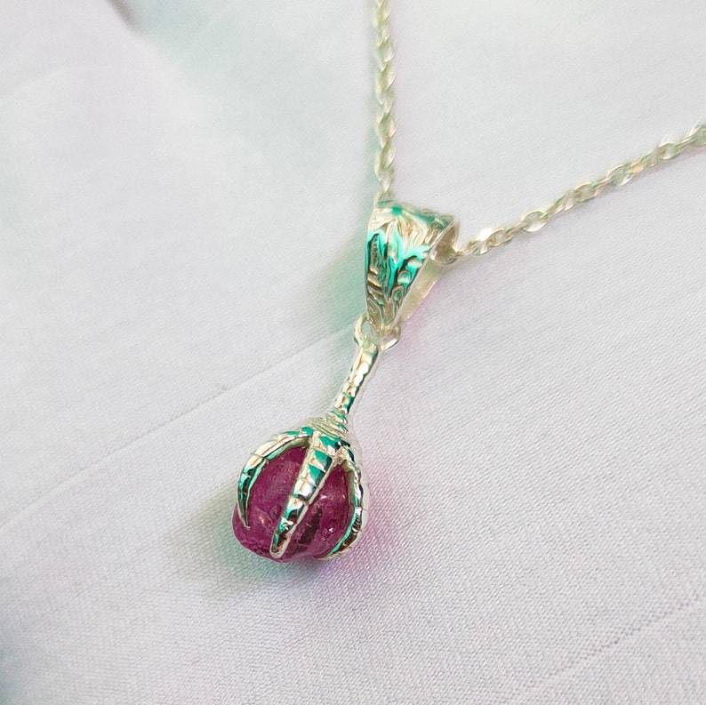 May include: A silver necklace with a pink gemstone pendant. The pendant is held in a silver claw design.
