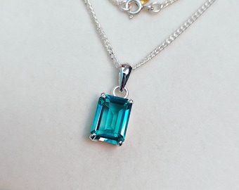 May include: A silver chain necklace with a pendant featuring a large, rectangular, emerald-cut blue gemstone.