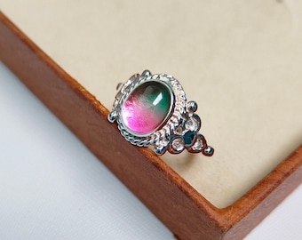 May include: A silver ring with a pink, green, and blue oval gemstone set in a decorative silver bezel. The ring has a delicate design with small silver accents.