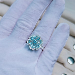 May include: A silver ring with a blue gemstone flower design. The ring is set with multiple small, round, blue gemstones and smaller, clear gemstones.