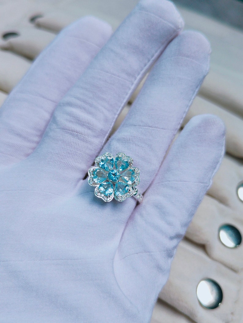 May include: A silver ring with a blue gemstone flower design. The ring is set with multiple small, round, blue gemstones and smaller, clear gemstones.