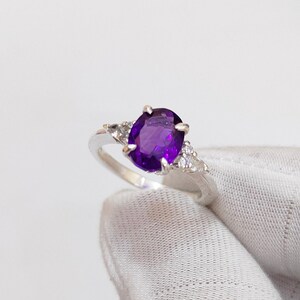 May include: A silver ring featuring a large oval amethyst gemstone, surrounded by smaller clear gemstones.