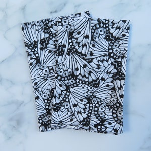 May include: Two white fabric napkins with a black and white butterfly pattern. The butterflies are arranged in a random pattern and are all different sizes.
