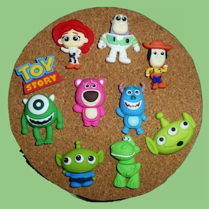 May include: A collection of colorful Toy Story character figurines, including Woody, Buzz Lightyear, and others, arranged on a round, brown corkboard. The "Toy Story" logo is also present. The figurines are brightly colored and detailed.