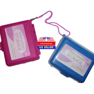 Peut inclure: Deux petites boîtes de rangement en plastique pour bijoux. L'une est rose et l'autre est bleue. Les deux portent l'inscription "Jewelry Essentials Storage".