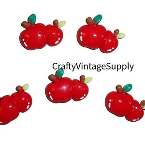 May include: Six red and green apple shaped embellishments. The apples are made of plastic and have a glossy finish. They are perfect for adding a touch of autumn to crafts.