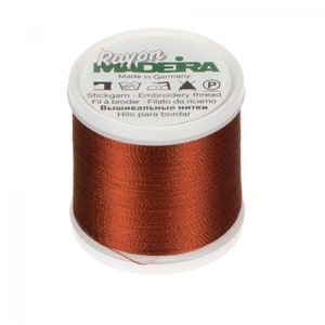 May include: A spool of brown embroidery thread with a white top. The label reads "Rayon MADERA" and "Made in Germany". The spool is filled with a shiny, tightly wound thread, perfect for various embroidery projects.