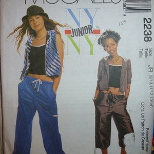 May include: McCall's NY Junior pattern 2238. The pattern features two young people wearing casual outfits. One is wearing blue pants and a vest, the other is wearing brown capri pants and a jacket. The pattern size is JR (9/10, 11/12, 13/14).