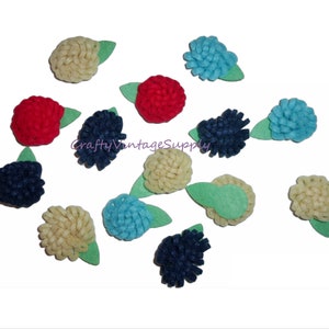 May include: Assortment of felt flower embellishments in various colors, including red, blue, cream, and navy blue. Each flower has a green felt leaf attached.