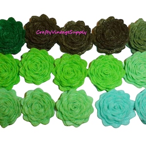 May include: A collection of felt flower embellishments in various shades of green, from deep forest to light teal. The flowers are arranged in rows, showcasing their layered petal design. The text "CraftyVintageSupply" is visible in the image.