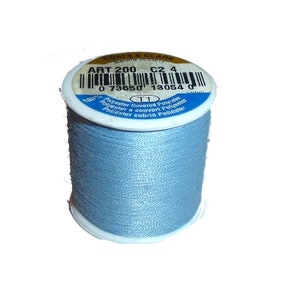 Könnte beinhalten: Eine Spule hellblauen Coats & Clark-Garnes mit der Aufschrift "Art 200 C2 4" und dem Barcode 0 73650 13054 0. Das Etikett trägt außerdem die Aufschrift "100% Polyester überzogen mit Polyester".