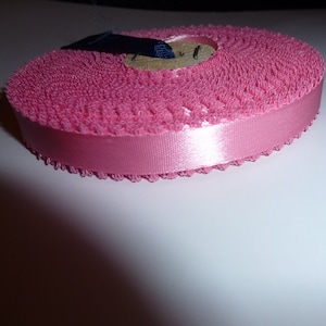 May include: Pink satin ribbon with a ruffled edge. The ribbon is rolled up and ready to be used for crafts or sewing projects.