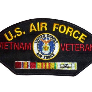 Puede incluir: Parche negro con el texto "U.S. AIR FORCE VIETNAM VETERAN" en letras amarillas y rojas. El parche presenta un emblema circular de la Fuerza Aérea de los Estados Unidos y una cinta con rayas de colores. El parche tiene forma de escudo.