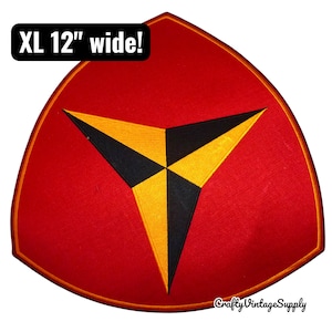 Puede incluir: Un parche rojo grande, XL de 30 cm de ancho, con un diseño geométrico amarillo y negro. El parche es triangular con un borde dorado y el texto "XL 12" wide!" en un cuadro negro.